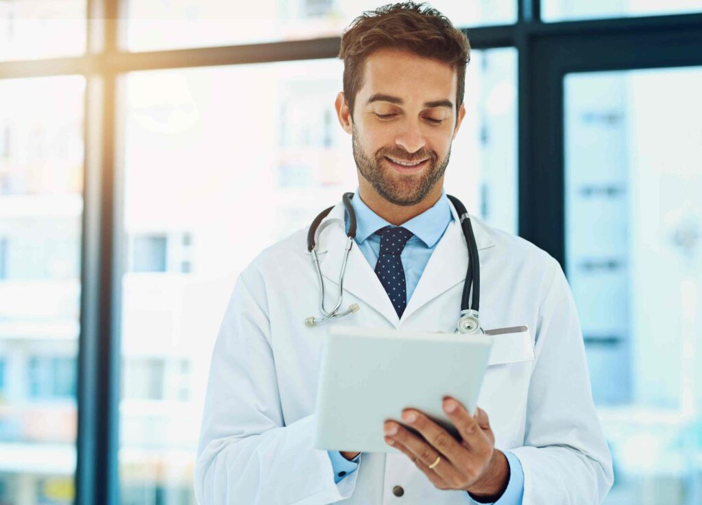 Arzt im weißen Kittel mit Stethoskop hält ein Tablet, symbolisiert die Fachsprachenprüfung Medizin in Deutschland.